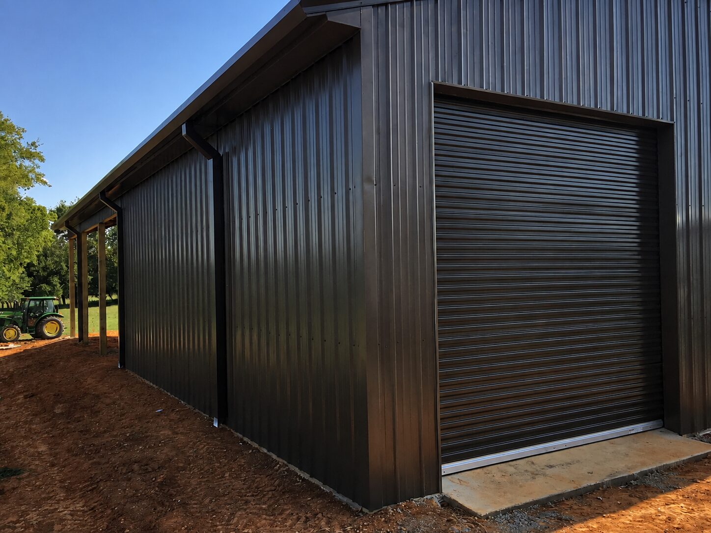 Dark bronze pole barn with roll-up door and open side shed
